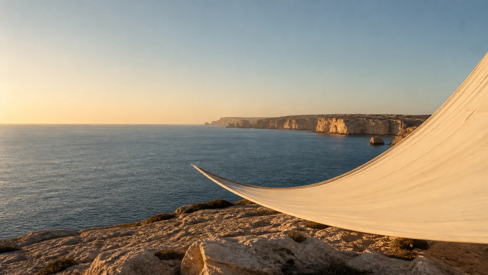 Warm morning light over the Algarve coast with a sculptural canvas sail